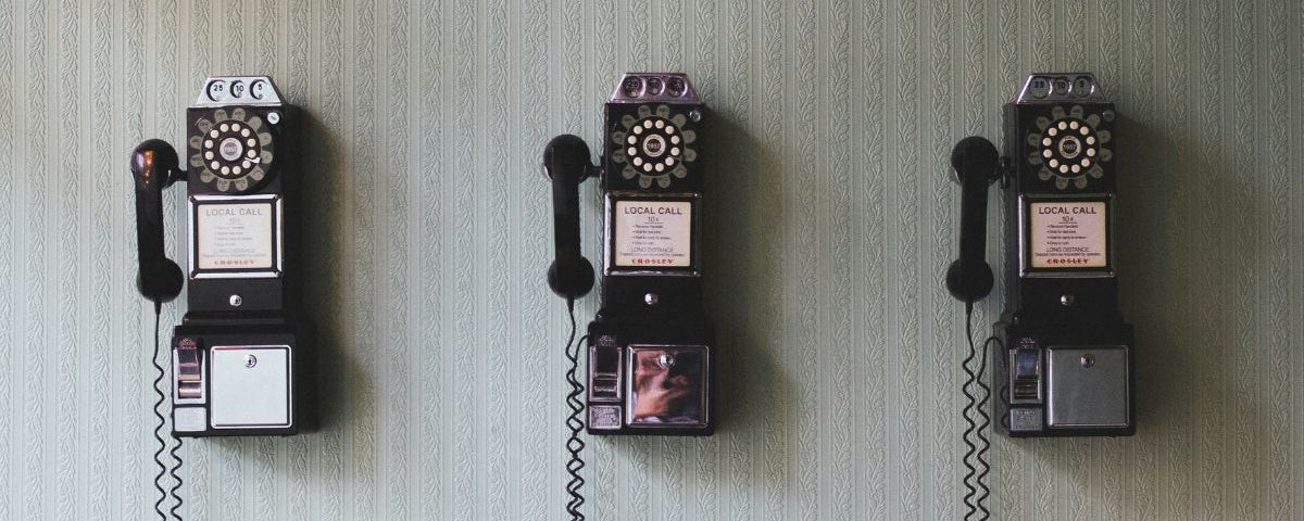 Three vintage wall telephones mounted on a textured wall.
